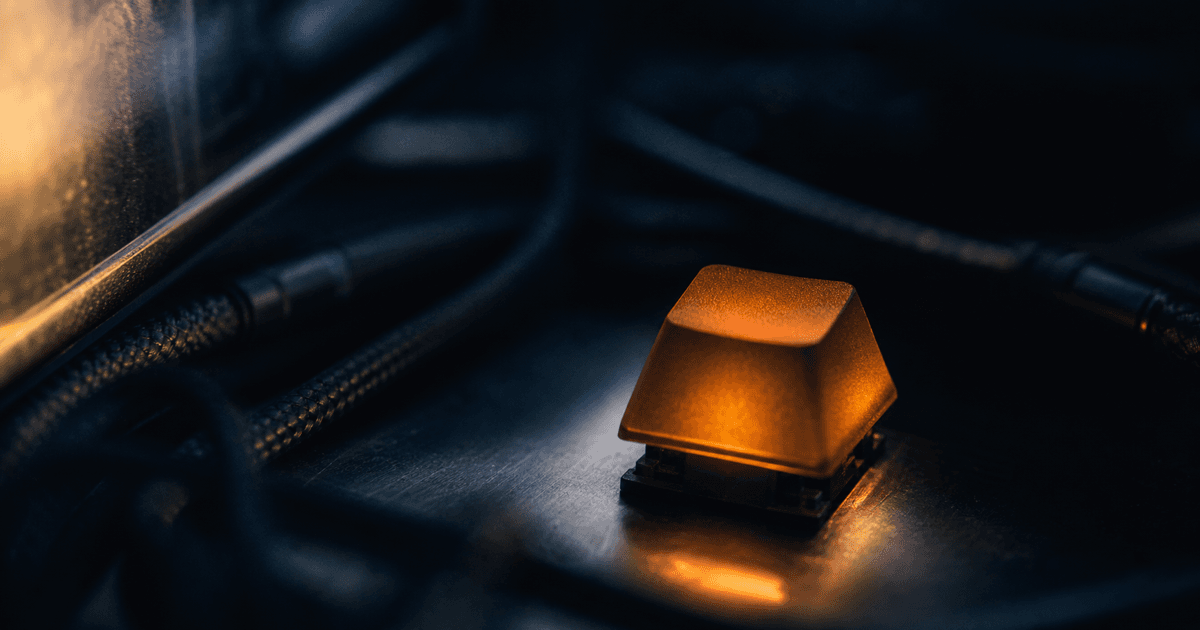 Close-up of a single illuminated mechanical keyboard key against dark cables and a reflected terminal screen